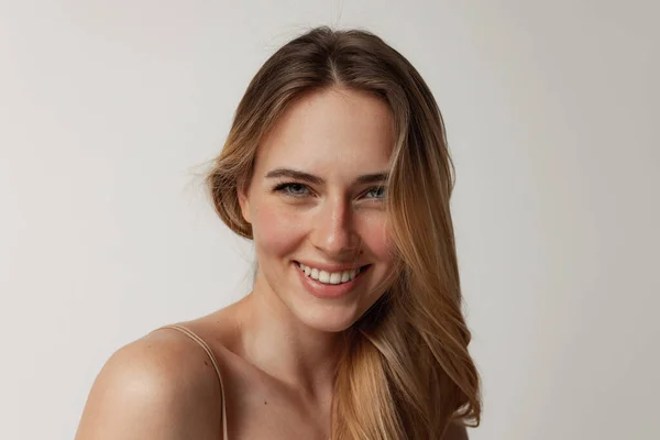 Portrait of tender young woman with perfect face smiling at camera, posing isolated over grey studio background — Stock Photo, Image