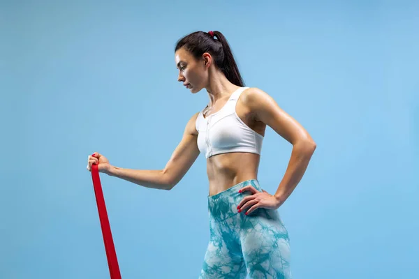 Μισού μήκους πορτρέτο της νεαρής αθλητικής γυναίκας κατάρτισης, κάνοντας ασκήσεις που απομονώνονται σε μπλε φόντο στούντιο — Φωτογραφία Αρχείου