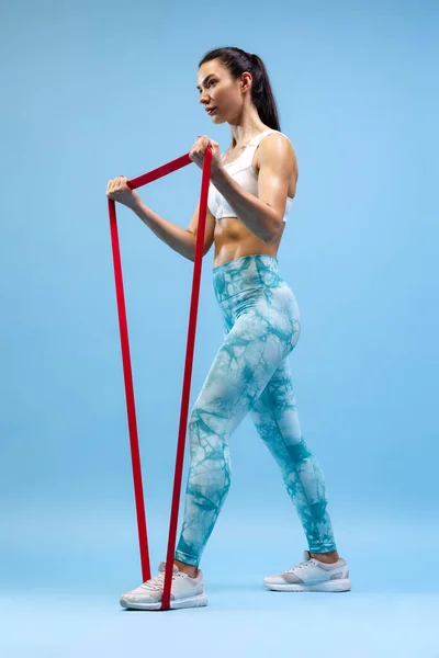 年轻女运动员训练的肖像，在蓝色工作室背景上孤立的上升的手肌肉 — 图库照片