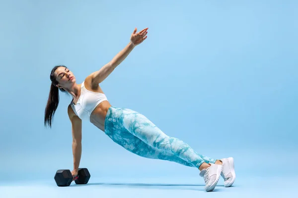 Retrato de una joven entrenadora deportiva, de pie sobre tabla lateral con mancuerna aislada sobre fondo azul del estudio — Foto de Stock