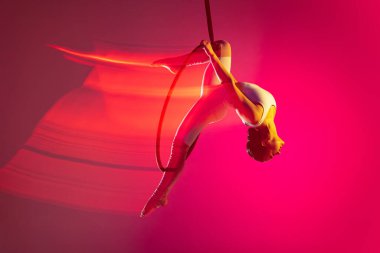 Genç, esnek bir kız, profesyonel hava jimnastikçisi, pembe arka planda karışık ışık efektiyle izole edilmiş performans sergiliyor.