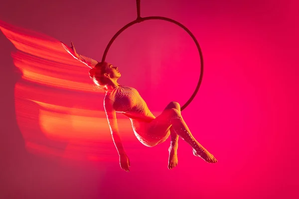 Young artistic girl, professional air gymnast training, performing isolated over pink background with mixed lights effect — Stok fotoğraf