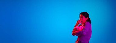 Portrait of young emotive girl with popcorn basket isolated over blue background in neon light. Excited movie.