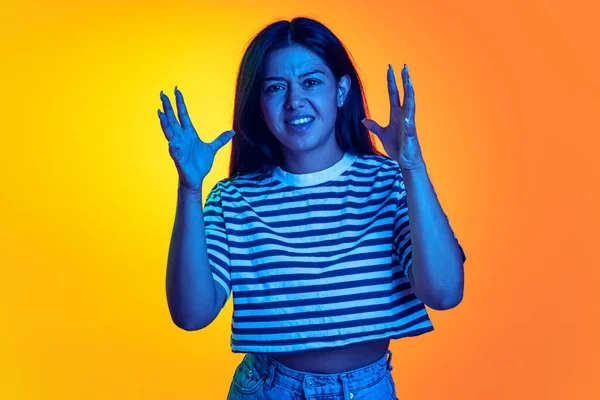 Portrait of young emotive girl showing irritation isolated over gradient orange yellow background in neon light —  Fotos de Stock