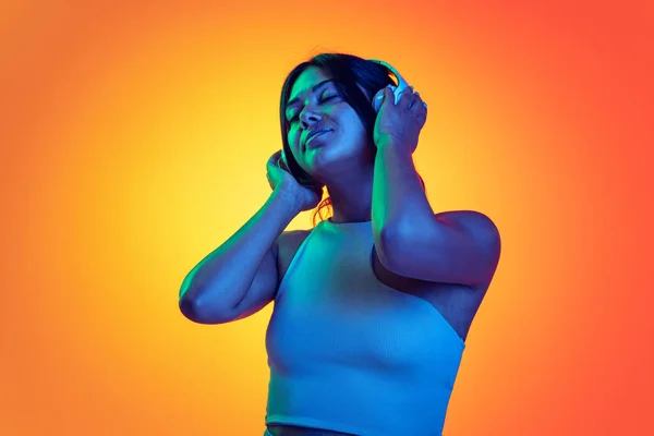 Turuncu arka planda, neon ışıkta izole edilmiş kafadanbacaklı müzik dinleyen genç bir kızın portresi. Memnuniyet — Stok fotoğraf