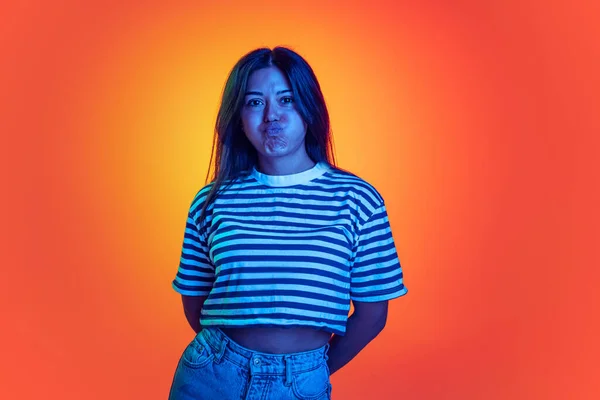Young emotive girl making funny face, blowing cheeks, posing isolated over orange background in neon light — Stok fotoğraf