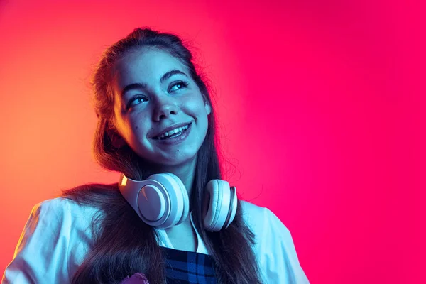 ネオンの光の中でピンクのスタジオの背景に隔離されたポーズをとるヘッドフォンを持つ若い女の子の肖像画。夢のような表情 — ストック写真