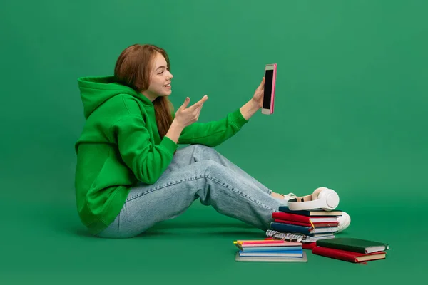 Portré fiatal lány, diák alkalmi ruha, kapucnis ül a padlón, amelynek online lecke tabletta elszigetelt zöld stúdió háttér — Stock Fotó