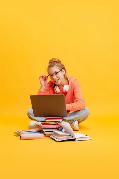 Retrato de menina, estudante de óculos e suéter sentado no chão, estudando isolado sobre fundo amarelo — Fotografia de Stock