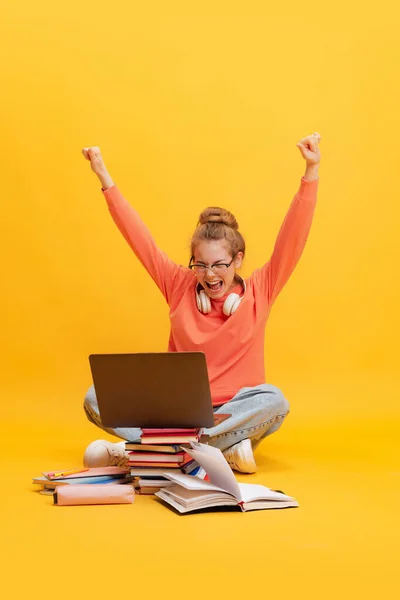Retrato de menina, estudante de óculos e suéter sentado no chão com laptop, estudando isolado sobre fundo amarelo. Tenho a maior marca. — Fotografia de Stock