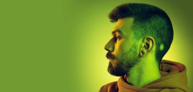 Yandan bakan genç adamın portresi, yeşil stüdyonun arka planında izole edilmiş bir poz.