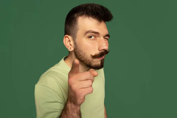 Portret van jonge stijlvolle man met snor kijken en wijzen naar camera, poseren geïsoleerd over groene studio achtergrond — Stockfoto