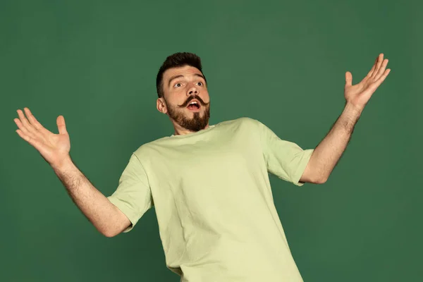 Πορτρέτο του νεαρού άνδρα με κομψό μουστάκι που δείχνει σοκαρισμένη έκφραση, απλώνοντας τα χέρια απομονώνονται σε πράσινο φόντο στούντιο — Φωτογραφία Αρχείου