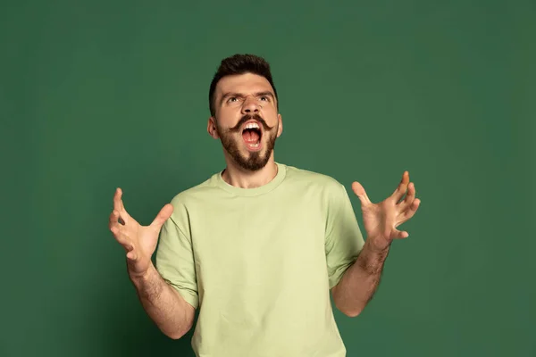 Προσωπογραφία του νεαρού συναισθηματικού άνδρα που δείχνει εκνευρισμό, ουρλιάζοντας απομονωμένος σε πράσινο φόντο στούντιο — Φωτογραφία Αρχείου