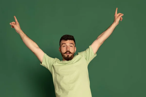 Portrait de jeune homme émotif au visage drôle posant isolé sur fond de studio vert. Temps de fête — Photo