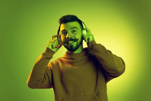 Πορτρέτο του νεαρού άνδρα με κομψό μουστάκι ακούγοντας μουσική σε ακουστικά που απομονώνονται σε πράσινο φόντο στούντιο — Φωτογραφία Αρχείου