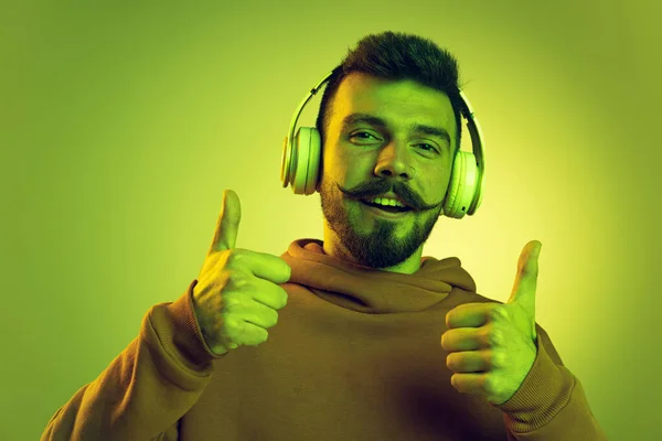 Portrait de jeune homme avec une moustache élégante écoutant de la musique dans des écouteurs isolés sur fond de studio vert — Photo