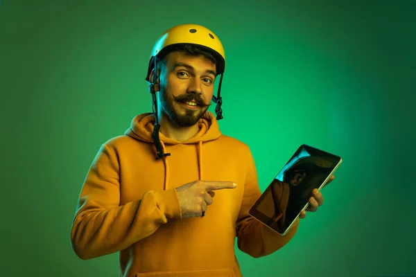 Portrait de jeune homme travaillant sur le service de livraison, tenant la tablette isolée sur fond de studio vert sous la lumière du néon. Dispositifs de dérivation — Photo