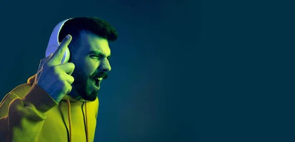 Πορτρέτο του νεαρού συναισθηματική άνθρωπος ακούγοντας δυναμική μουσική σε ακουστικά απομονώνονται σε μπλε φόντο σε νέον φως. Φλάιερ — Φωτογραφία Αρχείου