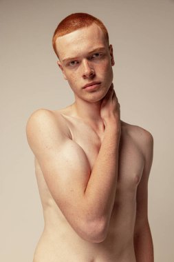 Gri stüdyo arka planında çıplak poz veren yakışıklı kızıl saçlı bir adamın portresi. Çilli bir model. Erkek güzeli. Erkek sağlığı, vücut ve cilt bakımı, yaşam tarzı, spor kavramı