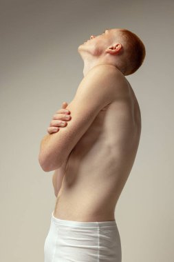 Gri stüdyo arka planında izole edilmiş beyaz iç çamaşırlı yakışıklı bir gencin yarım bacaklı portresi. Erkek modası. Kas modeli. Gençlik kavramı, özgüven, vücut ve cilt bakımı. Vücut sanatı