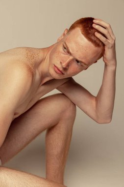 Gri stüdyo arka planında çıplak poz veren yakışıklı kızıl saçlı bir adamın portresi. Çilli vücut. Erkek güzelliği, moda, erkek sağlığı, sağlık, fitness, kozmetoloji kavramı