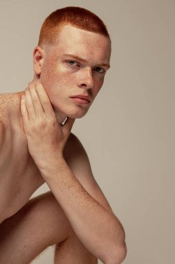 Gri stüdyo arka planında çıplak poz veren yakışıklı kızıl saçlı bir adamın portresi. Erkek güzelliği, moda, erkek sağlığı, sağlık, zindelik kavramı. Kameraya bakan bir model