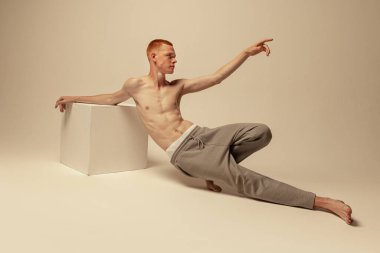 Gri stüdyo arka planında izole edilmiş pantolonsuz poz veren genç, kızıl saçlı bir adamın portresi. Sanat fotoğrafçılığı. Erkek güzelliği, moda, erkek sağlığı, sağlık, zindelik kavramı