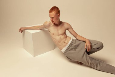 Gri stüdyo arka planında izole edilmiş pantolonsuz poz veren genç, kızıl saçlı bir adamın portresi. Kaslı, zayıf bir vücut. Erkek güzelliği, moda, erkek sağlığı, sağlık, zindelik kavramı