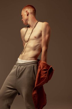 Kahverengi stüdyo arka planında izole edilmiş genç ve yakışıklı kızıl saçlı bir adamın portresi. Moda, tarz, beden estetiği, güzellik, erkek sağlığı kavramı