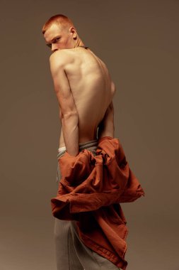 Kahverengi stüdyo arka planında izole edilmiş genç ve yakışıklı kızıl saçlı bir adamın portresi. Moda, tarz, beden estetiği, güzellik, erkek sağlığı kavramı