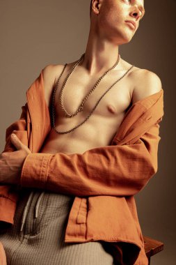 Kızıl saçlı, çilli, gömlekli bir adam kahverengi arka planda izole edilmiş. Sportif, kaslı vücut şekli. Moda, tarz, beden estetiği, güzellik, erkek sağlığı, fitness kavramı