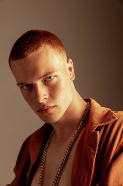 Kahverengi stüdyo arka planında izole edilmiş çilli yakışıklı kızıl saçlı genç adam portresi. Dikkatli bak. Moda, tarz, beden estetiği, güzellik, erkek sağlığı kavramı