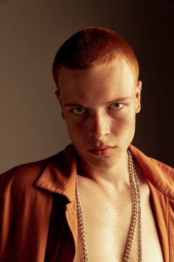 Yüzünde çilleri olan, kahverengi stüdyo arka planında izole edilmiş kızıl saçlı genç adamın yakın plan portresi. Derin bak. Moda, tarz, beden estetiği, güzellik, erkek sağlığı kavramı