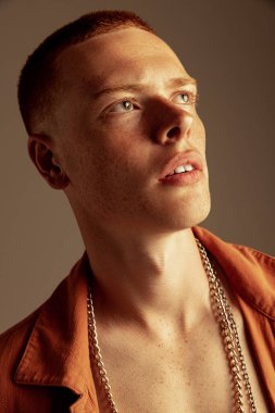 Yüzünde çilleri olan, kahverengi stüdyo arka planında izole edilmiş yakışıklı kızıl saçlı genç adamın yakın plan portresi. Moda, tarz, beden estetiği, güzellik, erkek sağlığı kavramı