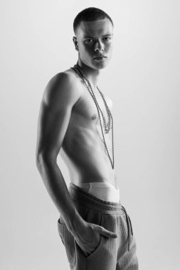 Şık, yakışıklı, üstsüz poz veren ve ciddi bir ifadeyle kameraya bakan genç adamın portresi. Siyah beyaz fotoğrafçılık. - Sanat. Moda, tarz, beden estetiği, güzellik, erkek sağlığı kavramı