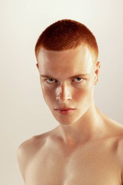 Çilli suratlı, genç, kızıl saçlı bir adamın portresi. Gri stüdyo arka planında izole edilmiş kameraya bakıyor. Erkek sağlığı, yaşam tarzı, güzellik, vücut ve cilt bakımı, moda kavramı