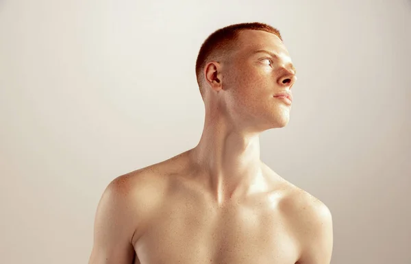 Portrait of young red-haired freckled man posing shirtless isolated over grey studio background. Concept of mens health, lifestyle, beauty, body and skin care. Textured collarbone.