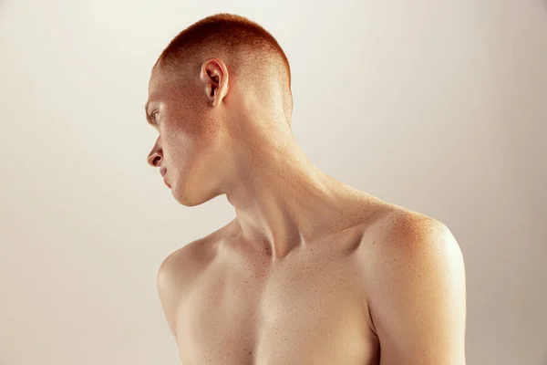Portrait of young red-haired man posing shirtless isolated over grey studio background. Textured collarbone. Concept of mens health, lifestyle, beauty, body and skin care. Model with freckles