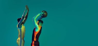 İki genç adamın portresi, zıplayan profesyonel basketbolcular, topu sepete atıyorlar mavi arka planda izole bir şekilde neon ışıkta. Spor anlayışı, takım oyunu, aksiyon, aktif yaşam tarzı, reklam