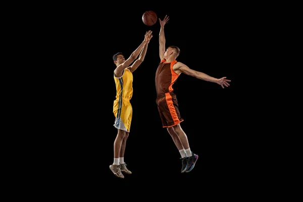 ジャンプで2人の若い男性 プロのバスケットボール選手のダイナミックな肖像画 黒のスタジオの背景に隔離されたバスケットにボールを投げます スポーツ チームゲーム アクション アクティブライフスタイル 広告の概念 — ストック写真