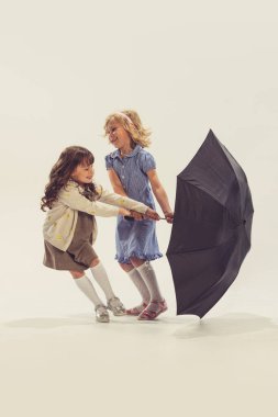 İki güzel kızın portresi, büyük siyah şemsiyeyle oynayan çocuklar, gri stüdyo arka planında izole edilmiş eğleniyorlar. Çocukluk kavramı, arkadaşlık, aile, eğlence, yaşam tarzı, eski moda