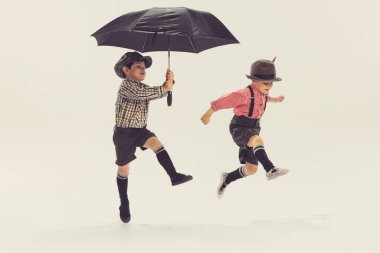 İki aktif küçük çocuğun portresi, şemsiyeyle oynayan çocuklar, gri stüdyo arka planında izole bir şekilde atlamak. Çocukluk kavramı, arkadaşlık, aile, eğlence, yaşam tarzı, eski moda