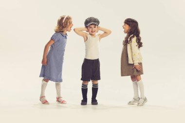 Birlikte oynayan üç çocuğun portresi, gri stüdyo arka planında izole edilmiş kulakları olan çocuğa bağıran kızlar. Çocukluk kavramı, arkadaşlık, aile, eğlence, yaşam tarzı, eski moda