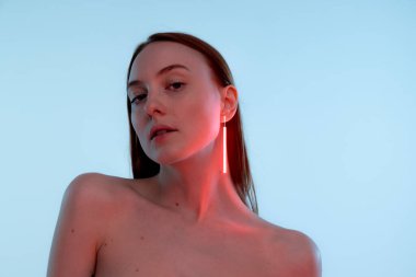 Neon renkli aksesuarları olan, poz veren, mavi arka planda izole edilmiş kameraya bakan genç bir kızın portresi. Güzellik, yaratıcılık, sanat, sayısallaştırma, moda eğilimleri kavramı