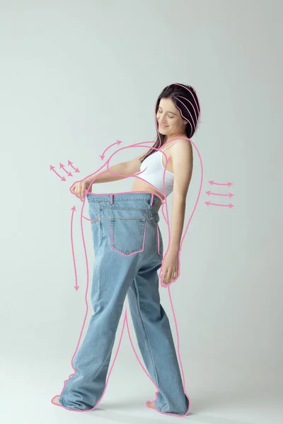 身穿内衣裤的瘦女人的画像 穿着超大号牛仔裤 灰色背景与之隔离 减肥前身体周围的线条 健康饮食 广告的概念 — 图库照片