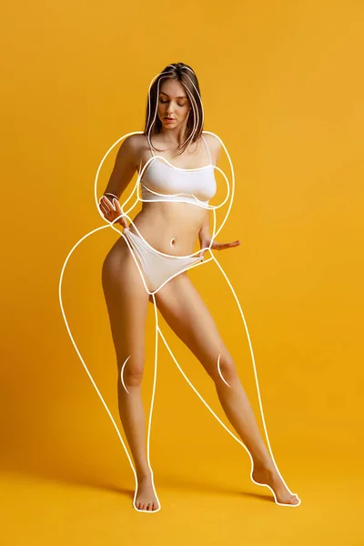 Beautiful woman with fit body in inner wear posing isolated over yellow studio background. Line doodles around body. Healthy lifestyle. Concept of healthy eating, dieting, loosing weight, fitness, ad