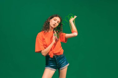 Yeşil stüdyo arka planında izole edilmiş oyuncak ile poz veren sıradan yaz kıyafetleri, şortu ve tişörtü giymiş güzel bir kızın portresi. Gençlik kavramı, güzellik, yaşam tarzı, moda, eğlence, duygular