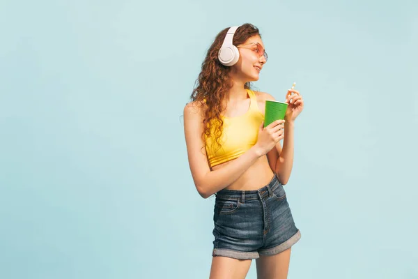 夏服の少女の肖像画 白いヘッドフォンのポーズ 青のスタジオの背景に隔離されたレモネードを飲む 美しさ ライフスタイル ファッション 楽しさ 感情の概念 — ストック写真