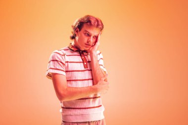 Düşünceli genç bir adamın portresi, turuncu stüdyo arka planında, neon ışıkta izole bir şekilde poz veriyor. Düşünceli bir bakış. Gençlik kavramı, moda, yaşam tarzı, duygular. İlan için alanı kopyala